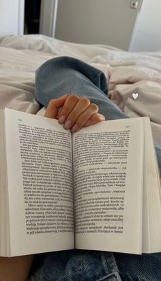 a person laying in bed reading a book with their hands on top of the book