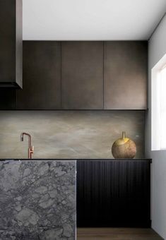 a modern kitchen with marble counter tops and black cabinetry, along with a gold faucet