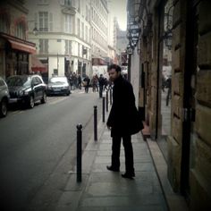 a man standing on the side of a street next to tall buildings and parked cars