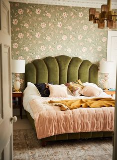 a green headboard on a bed in a room with floral wallpaper and pink bedspread