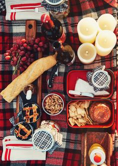 an assortment of food is laid out on a plaid tablecloth with candles and wine