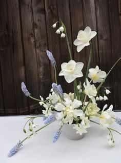 a vase filled with white and blue flowers on top of a table next to a wooden fence