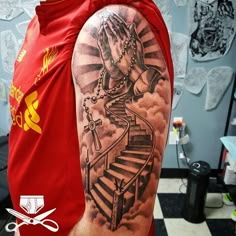 a man with a tattoo on his arm is standing in front of a staircase and holding hands up to the sky