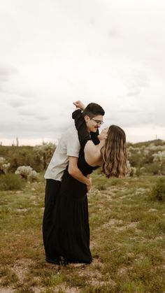 a man and woman are kissing in the middle of an open field with bushes behind them