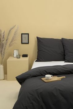 a bed with green sheets and pillows next to a white nightstand in a yellow room