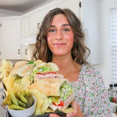 a woman holding a tray full of sandwiches and chips