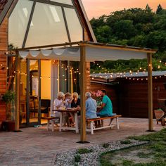 a group of people sitting at a picnic table in front of a house with string lights