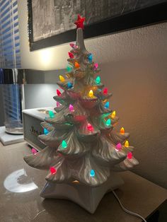 a white ceramic christmas tree with multicolored lights on it's base, sitting on a table