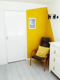 a chair sitting in front of a yellow wall next to a white dresser and door