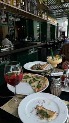 pizza and drinks are on the table in a restaurant with people sitting at the bar