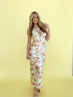 a woman standing in front of a yellow background wearing a floral print dress and sandals