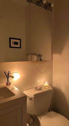 a white toilet sitting next to a sink under a bathroom mirror with candles on it