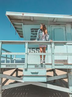 a woman standing on the top of a life guard tower with her hands in her pockets