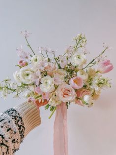 a person holding a bouquet of flowers in their hand with a pink ribbon tied around it