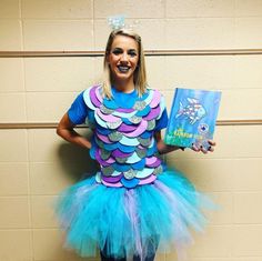 a girl in a blue and purple costume holding a book while standing against a wall