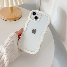 a person holding an iphone case on top of a white table next to a lamp