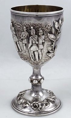 an ornate silver goblet with figures on it's sides and flowers in the center