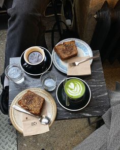 a table topped with plates and cups of coffee next to two slices of toast on top of each other