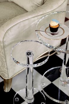 a cupcake sitting on top of a glass table next to a white chair and black and white checkered floor