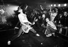 black and white photograph of young men playing guitar in front of an audience at a concert