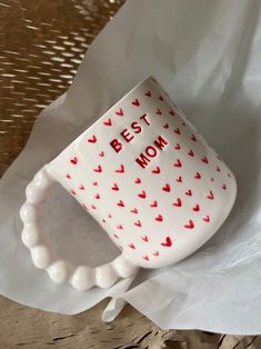 a white coffee cup with red hearts on it and the words'best mom'printed on it