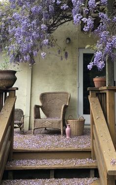 wicker chairs and wicker baskets are on the steps leading up to a porch with purple flowers