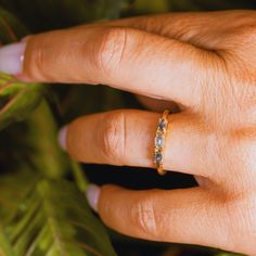 a woman's hand with a yellow gold ring on top of her finger and green leaves in the background