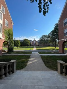 an empty walkway between two brick buildings in the middle of a grassy area with trees on both sides