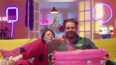 a man and woman sitting on a couch in front of a pink bowl with food