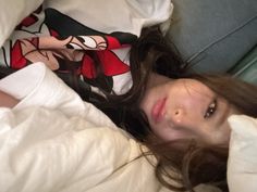 a woman laying in bed with white sheets and mickey mouse on her shirt, looking at the camera