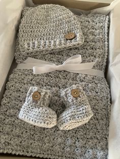 a crocheted baby blanket and booties set in grey with white bows on top