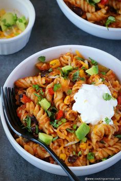 two white bowls filled with pasta and vegetables, topped with sour cream on the top