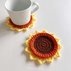 two crocheted coasters sitting on top of a table next to a cup