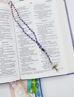 an open book with a rosary on top of it next to some ribbons and beads