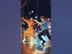 two people dancing in the street at night with stars on the ground and one person wearing an orange outfit