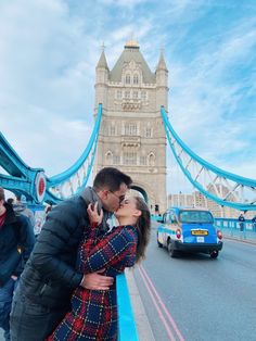 a man and woman kissing in front of the tower bridge with cars passing by them