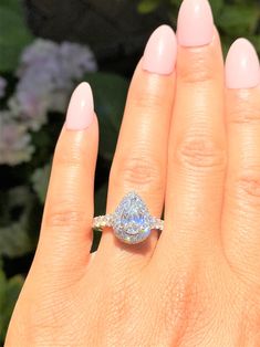 a woman's hand with a diamond ring on top of her finger and flowers in the background