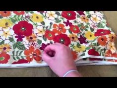 someone is cutting fabric with scissors on the floor next to a flowered cloth that has red, yellow and green flowers