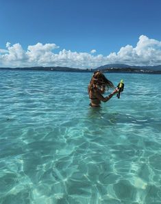 a woman is in the water holding a bottle with a bird perched on it's arm