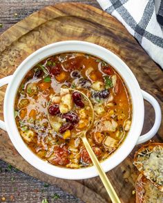 a white bowl filled with soup and bread on top of a wooden cutting board next to a spoon