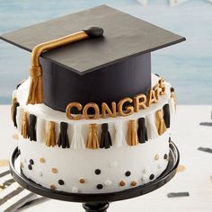 a graduation cake with the word congrat written on it and tassels in gold