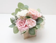 a vase filled with pink and white flowers on top of a wooden block covered in greenery