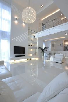 a living room with white furniture and chandelier hanging from the ceiling in front of a flat screen tv