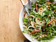 a salad with apples and nuts in a white bowl on a wooden table next to utensils