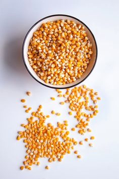 a bowl filled with corn on top of a white table next to a pile of kernels