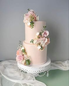 a three tiered wedding cake with pink flowers on top and white lace around the edges