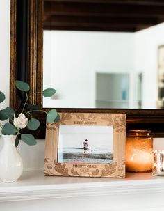 there is a vase with flowers and candles on the mantle next to a framed photo