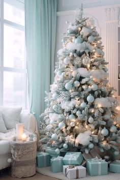 a white christmas tree with blue and silver presents under it in front of a window