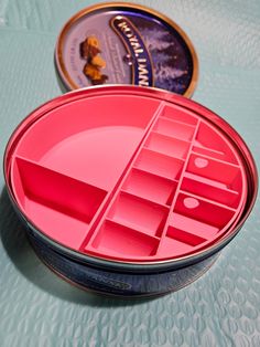 a pink container with compartments sitting on top of a table next to a tin of food