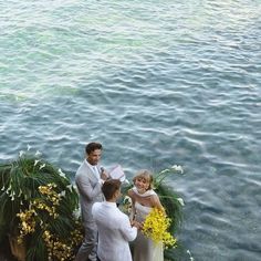 a man and woman standing next to each other in front of flowers on the water